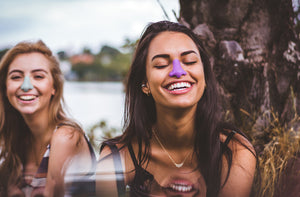 Two young girls laughing and wearing NOZ sunscreen in vibrant colors to protect their nose for UV Rays.